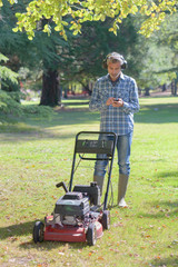 Man stood by lawnmower using smartphone