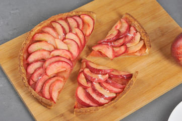 Apple open pie on a light wooden board. The cake is cut into pieces. Gray background. Close-up. View from above.