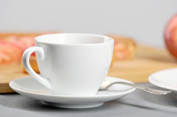 White cup and saucer. On a saucer a teaspoon. In the background is an apple pie. Light background. Close-up.