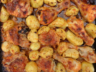 oven-baked chicken with potatoes and tomato sauce and spices on a tray