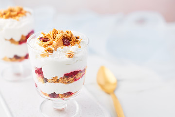 Close up of healthy raspberry yogurt parfait in a glass with golden spoon on white marble table over pink background with copy space.