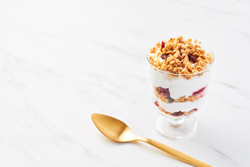 Healthy raspberry yogurt parfait in a glass with golden spoon on white marble table with copy space. Top view.