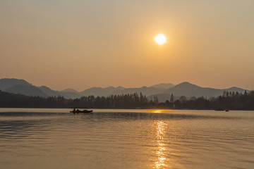 Boat traveling on West Lake under sunset in Hangzhou