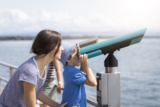 Germany, Friedrichshafen, Lake Constance, mother with son looking through telescope at lakeshore