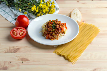 Italian spaghetti with a meat based sauce in a plain white plate on wooden table. Spaghetti pasta with tomatoes.