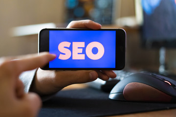 young male worker holding a smartphone with SEO text design in the office, search engine optimization concept f