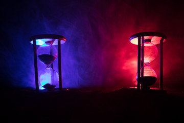 Time concept. Silhouette of Hourglass clock and smoke on dark background with hot yellow orange red blue cold back lighting