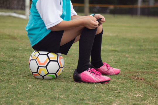 A soccer player sitting on the ball. 