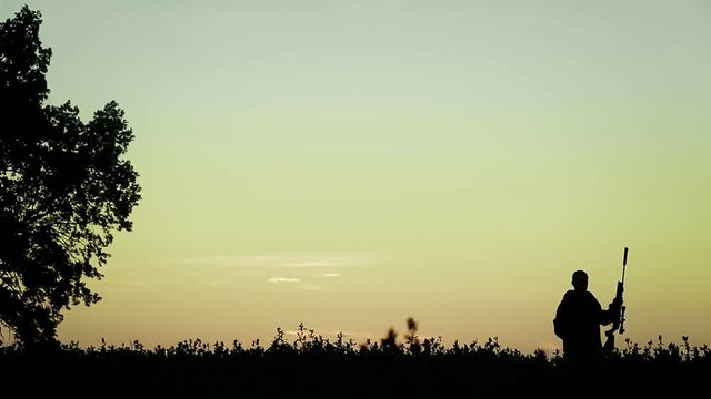 Hunter at sunset stands with a gun on his shoulder