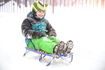 Fototapeta na wymiar Adorable child boy riding a sled from a snow slide.