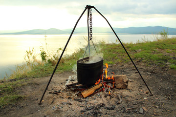 Cooking in a pot on a fire on the shore of the lake. Close-up. Landscape. Background.