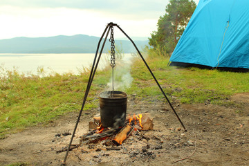 Tent and bowler on the fire on the shore of the lake. Landscape. Background.