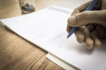 Contract signature in faded high quality with pen in hand on wooden desk.