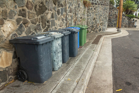 Trash bins in line on street for garbage pickup.  Organized recycling and pickup containers on road.