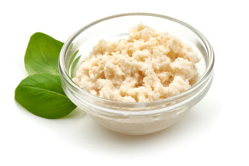Grated horseradish sauce in small glass bowl with basil leaves, close-up, isolated on white background.