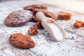 Cookies with chocolate slices sprinkled with powdered sugar and a wooden measuring spoon. Fresh pastry on wooden background.