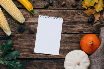 Autumn mood: white notebook, pumpkins and corn with yellow leaves on a wooden background