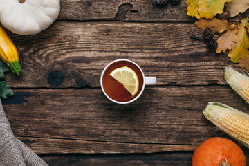 Autumn vegetables:tea, pumpkins and corn with yellow leaves on a wooden background