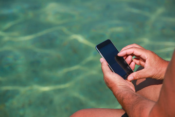 A man holding smartphone while sitting on the seaside pier.