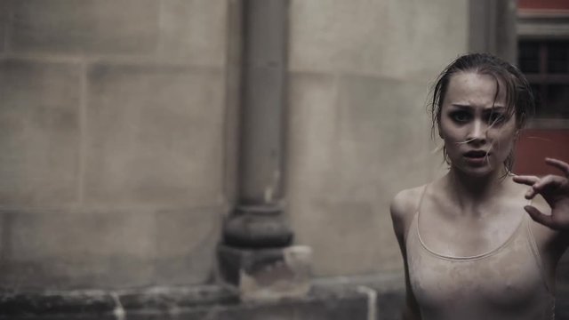 Young professional female dancer is performing acrobatic dance along the medieval street under the rain. Ballerina dancing in water drops, slow motion