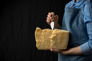 Woman holding knife and a slice of parmesan cheese on black background
