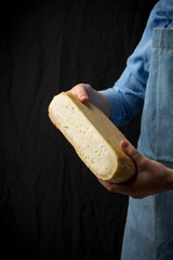 Woman in blue apron holding taleggio cheese on dark background