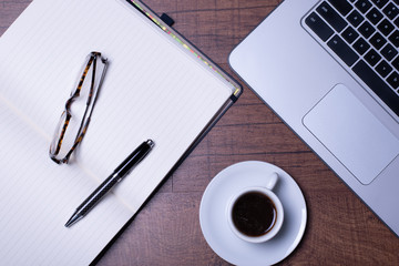 Woodgrain Table with Computer, espresso coffee in a white cup on a white saucer, Glasses, Pen and Notebook.