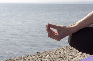 Young attractive woman doing yoga outdoors on the river bank. Lotus pose and hands closeup