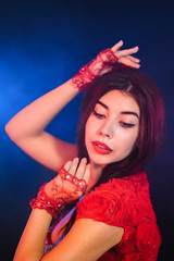 Fototapeta premium Tempting sexy traditional oriental belly dancer girl dancing on purple neon smoke background. Woman in exotic red costume sexually moves her semi-nude body.