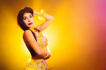 Alluring sexy traditional oriental belly dancer girl dancing on yellow neon smoke background. Woman...