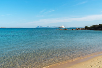 View on the beach with green-blue still water and footprints on the orange-yellow sand with a large white yacht boat on the horizon in natural light at noon