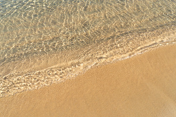 Beachline with bright orange-yellow sand and still transparent sea water in natural light at noon