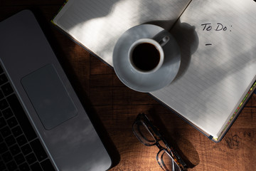 Woodgrain Table with Computer, espresso coffee in a white cup on a white saucer, Glasses, Pen and Notebook.