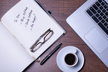 Woodgrain Table with Computer, espresso coffee in a white cup on a white saucer, Glasses, Pen and Notebook.