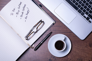 Woodgrain Table with Computer, espresso coffee in a white cup on a white saucer, Glasses, Pen and Notebook.