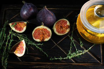 Ripe figs are sliced on a dark wooden board next to a sprig of thyme for tea and a jar of linden honey
