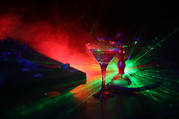 Glass with martini with olive inside on dj controller in night club. Dj Console with club drink at music party in nightclub with disco lights.