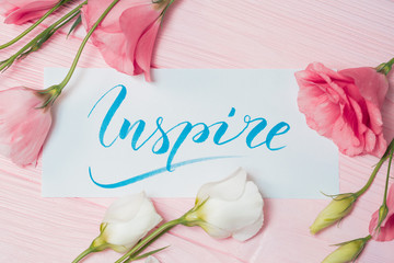 Inspire text. Font of lettering motivational word on white canvas with blue ink. Flowers eustoma...