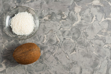 Coconut near heap of coconuts flakes in glass plate on old gray concrete with copy space. Flat lay