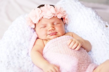 Cute and adorable newborn Caucasian girl smiling in her sleep. Pink head band with flowers and a light blanket, newborn photo session concept.