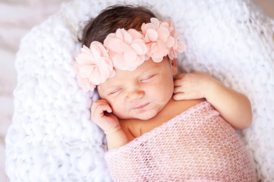 Cute and adorable newborn Caucasian girl smiling in her sleep. Pink head band with flowers and a light blanket, newborn photo session concept.