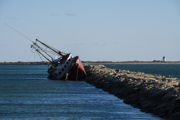 Boat Sinks at Rock Seawall with a Lighthouse in Near Distance