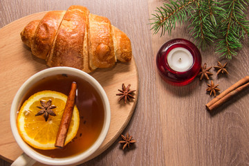 Obraz na płótnie Canvas A cup of tea with a croissant on a wooden background with New Year's decor