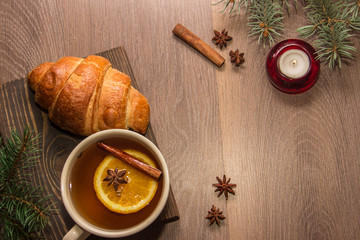 A cup of tea with a croissant on a wooden background with New Year's decor