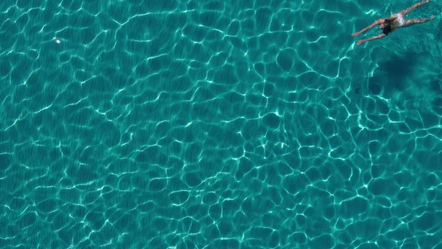 Aerial - Young woman in white bikini swimming underwater in crystal clear water