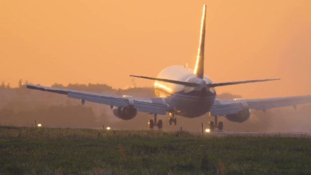 Airplane is landing to the runway at sunset. Back view