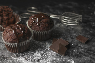 Close up of cocoa muffins with chocolate icing on rustic table covered with sugar and cocoa with...