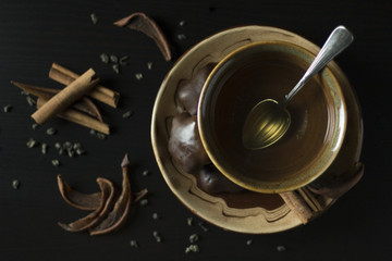 Close up of brown ceramic cup with hot green tea with gingerbread cookies, dried pears and cinnamon on dark background from above
