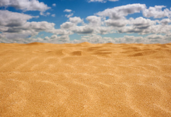 Fototapeta na wymiar Golden sand in the hot and sunny desert. Yellow sand against the blue sky with clouds.