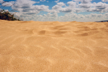 Golden sand in the hot and sunny desert. Yellow sand against the blue sky with clouds.